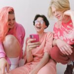 Three teenage friends laughing together while looking at a smartphone indoors