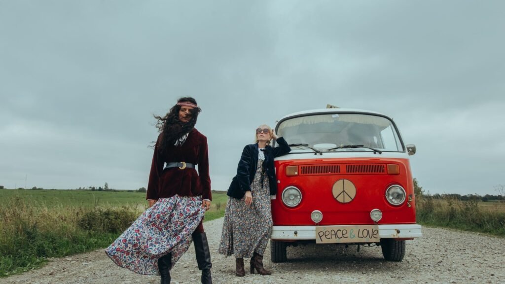 Two women in hippie outfits beside a vintage red van decorated with peace symbols