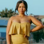 Confident plus-size woman in a yellow dress posing outdoors