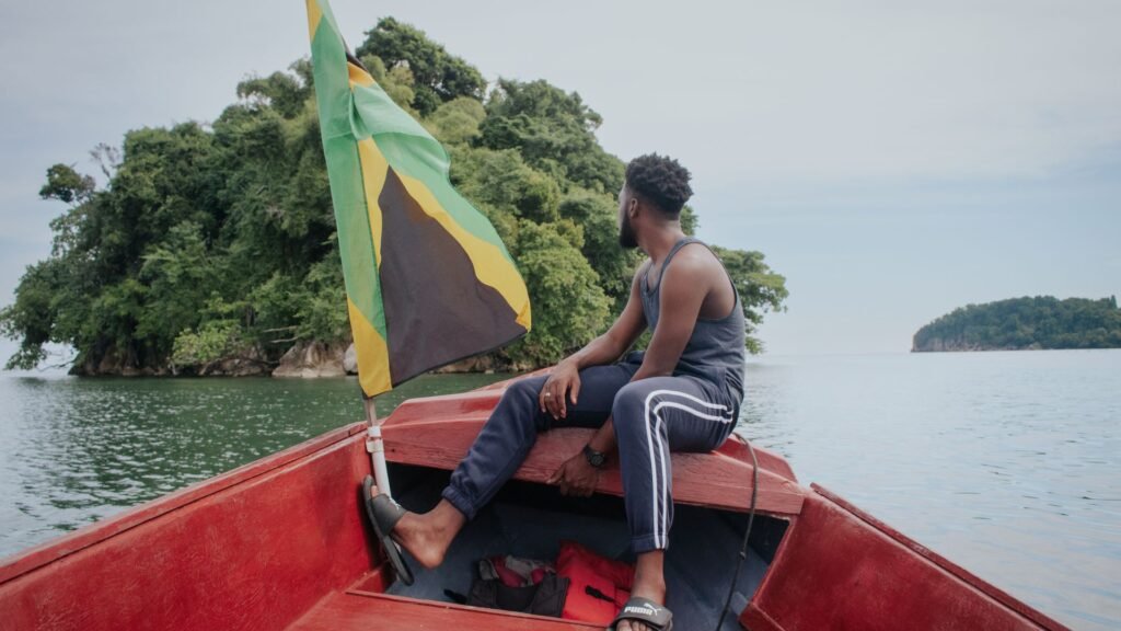 Man sitting on a boat with the Jamaican flag near a lush island