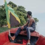 Man sitting on a boat with the Jamaican flag near a lush island