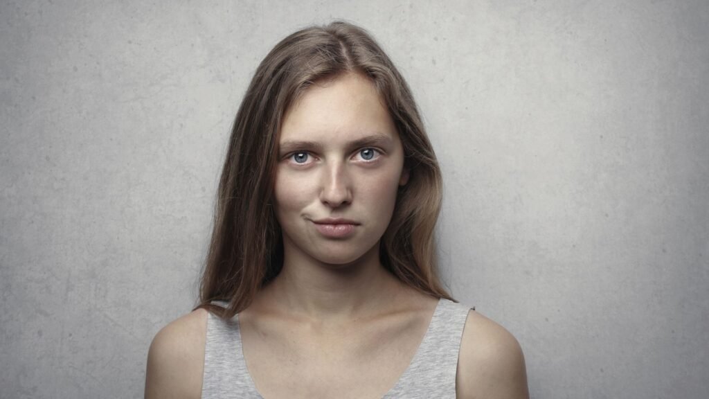 Portrait of a confident young woman with a playful, knowing smirk against a gray background, the classic arch expression