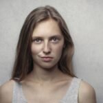Portrait of a confident young woman with a playful, knowing smirk against a gray background, the classic arch expression