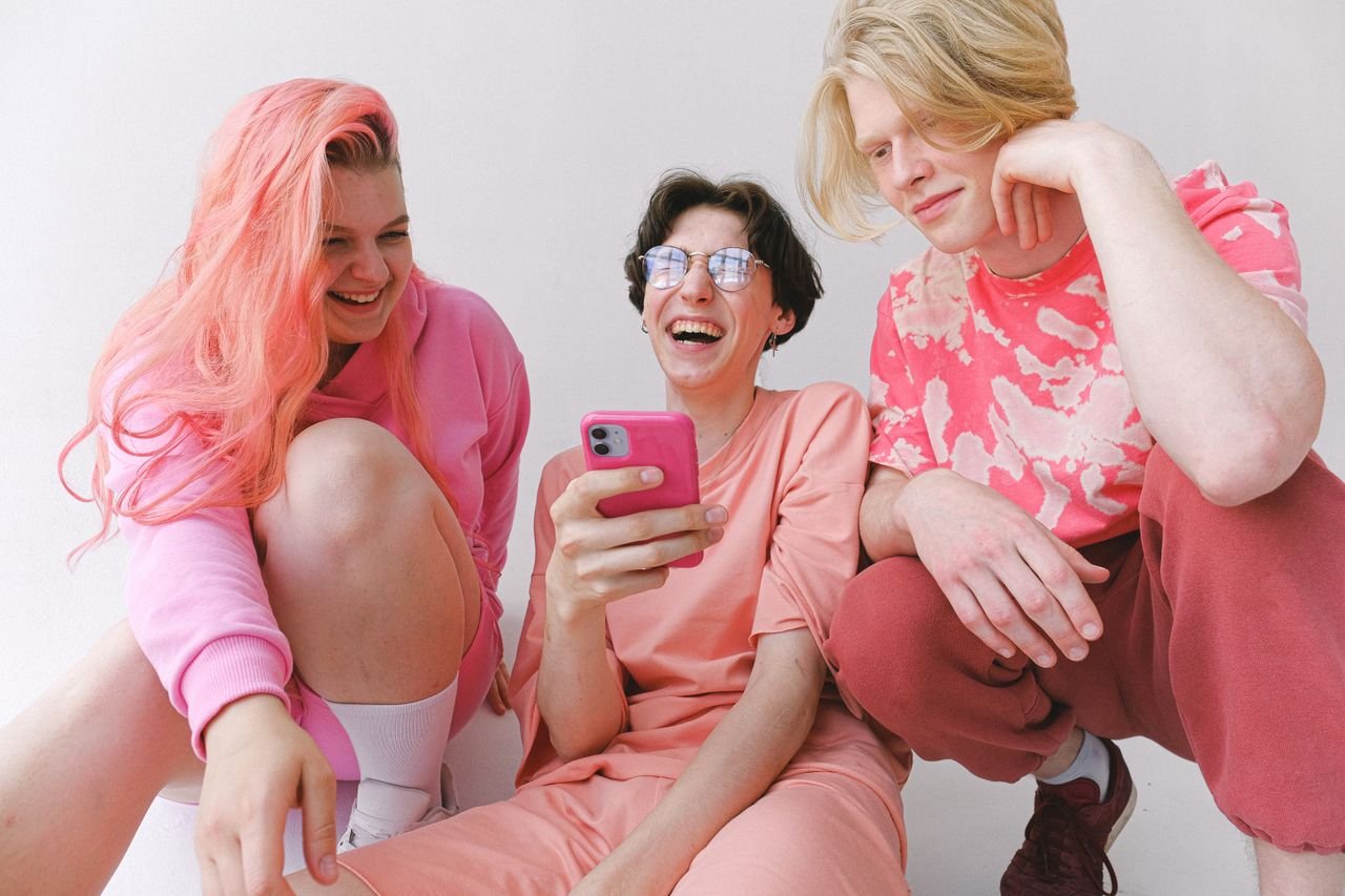 Three friends laughing while looking at a smartphone screen together, the casual setting where ASF slang is used most
